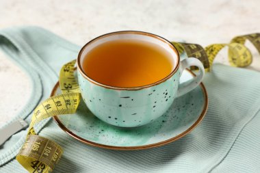 Bir fincan diyet çay, mezura ve arka planda şık spor bluzu. Kilo verme konsepti