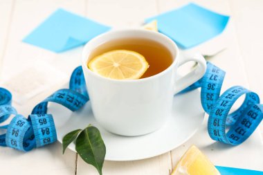 Kilo vermek için bir fincan çay ve beyaz ahşap masada şerit.