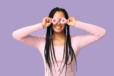 Güzel bir Afro-Amerikalı kadın mor arka planda gözleri kasımpatı çiçeğiyle kaplıyor.