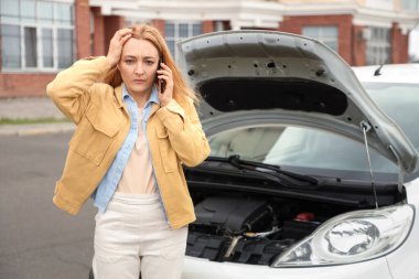 Bozuk arabanın yanında cep telefonuyla konuşan sinirli olgun bir kadın.