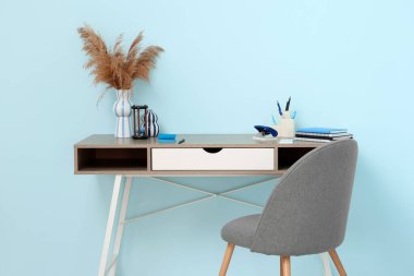 Rahat ofisteki mavi duvarın yanında vazo dolusu pampa, kırtasiye ve kum saati olan şık bir iş yeri.