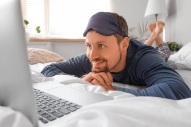 Evde dizüstü bilgisayarı olan pijamalı mutlu bir genç.