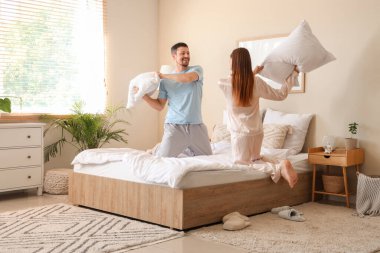 Evde pijamalı, yastık kavgası yapan genç bir çift.