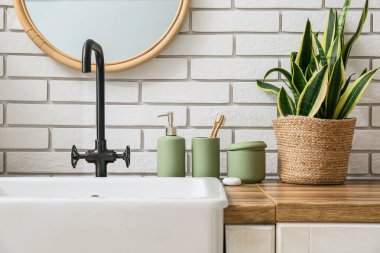 Banyo aksesuarları ve modern lavabo banyodaki beyaz tuğla duvarın yanındaki masada.