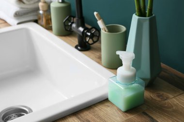 Banyoda yeşil duvarın yanındaki ahşap masada farklı banyo aksesuarları.