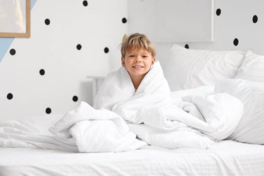 Pijamalı, battaniyeli, evde yatağında oturan tatlı, mutlu bir çocuk.