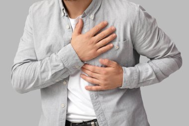 Gri arka planda kalp krizi geçiren genç adam, yakın plan.