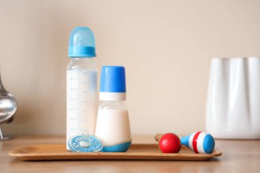 Bebek sütü formülü şişeleriyle dolu tepsi, duvarın yanındaki ahşap masada çıngırak ve emzik.