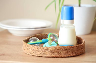 Bebek sütü formülü, çıngırak, emzik ve tabaklar ile ahşap mutfak tezgahında hasır tepsi