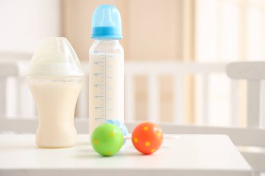 Bebek sütü formülü şişeleri ve çocuk odasındaki ışık masasında çıngırak.