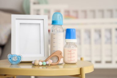 Bebek sütü formülü, emzik, ip ve boş resim çerçevesi çocuk odasındaki masada.