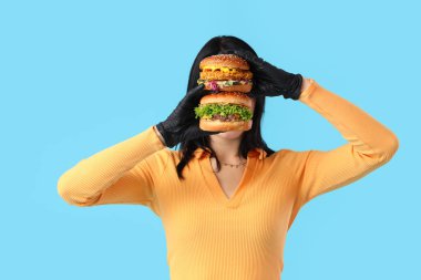 Mavi arka planda lezzetli burgerleri olan güzel genç bir kadın.