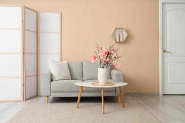 Sıcak kanepe ve vazodaki manolya çiçekleri oturma odasının içindeki sehpanın üzerinde.