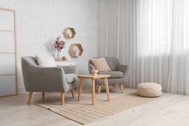 Koltuklar, sehpa ve çekmeceler. Odada manolya çiçekleri.