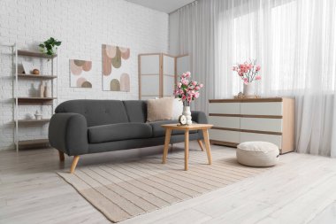 Rahat bir kanepe, sehpa ve odada manolya çiçekleri olan çekmeceler.