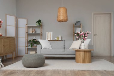 Oturma odasının içinde kanepe, masa ve vazoda manolya çiçekleri var.