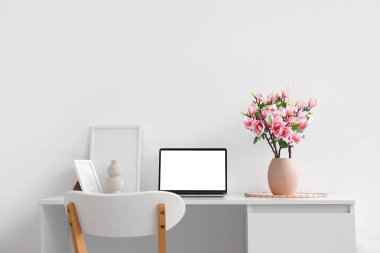 Işık duvarının yanındaki masanın üzerinde manolya çiçekleri olan vazo.