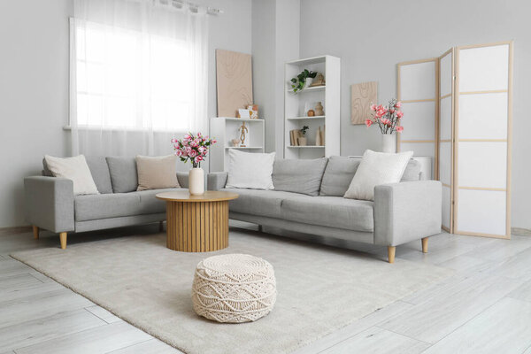 Cozy sofas and magnolia flowers in vase on coffee table in room