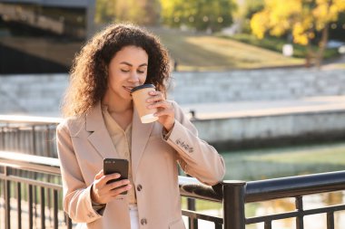 Güzel, mutlu, Afro-Amerikalı bir iş kadını cep telefonu ve bariyerin yanında bir fincan kahve ile.