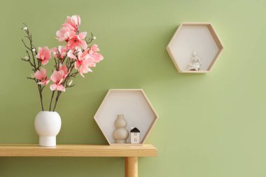 Masasında manolya çiçekleri ve yeşil duvarın yanında rafları olan bir vazo.