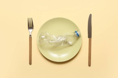 Masa ayarı ve sarı arka planda kullanılmış plastik su şişesi. Mikro Plastik Farkındalık Ayı