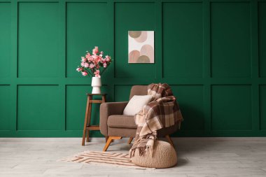 Koltuk, puf ve odada yeşil duvarın yanındaki manolya çiçekleriyle dur.