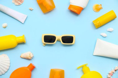 Mavi arka planda güneş kremi, güneş gözlüğü ve deniz kabukları olan kompozisyon