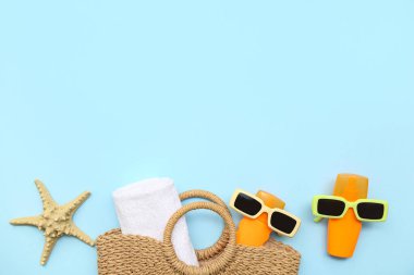 Mavi zemin üzerinde güneş kremi, güneş gözlüğü, çanta, denizyıldızı ve havlu bulunan kompozisyon