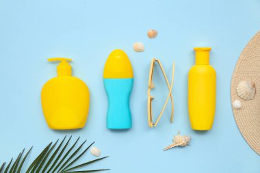 Güneş kremi, güneş gözlüğü, palmiye yaprağı ve mavi arka planda deniz kabukları olan kompozisyon