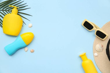 Güneş kremi, güneş gözlüğü, palmiye yaprağı ve mavi arka planda deniz kabukları olan kompozisyon