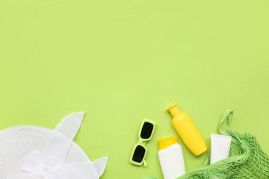 Yeşil arka planda güneş kremi, güneş gözlüğü, şapka ve ip torbası olan kompozisyon