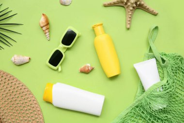 Yeşil arka planda güneş kremi, güneş gözlüğü, şapka ve ip torbası olan kompozisyon