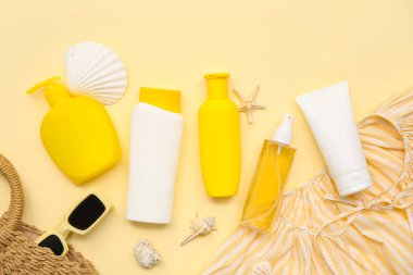 Bej arka planda güneş kremi, deniz kabuğu, bluz ve güneş gözlüğü şişeleri.