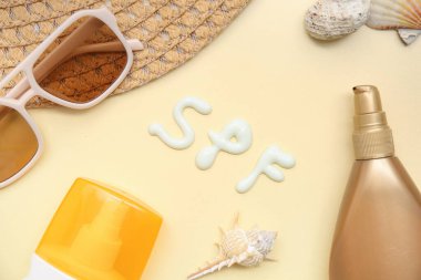 Güneş kremi şişeleri, güneş gözlüğü, şapka ve bej arka planda kremadan yapılmış kelime SPF ile kompozisyon
