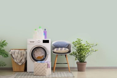 Çamaşır makinesi, sepet ve sandalyeli çamaşır odasının içi.