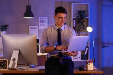 Genç işadamı geceleri ofiste dizüstü bilgisayarla çalışıyor.