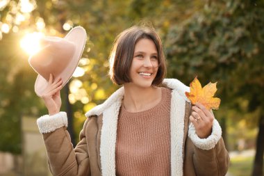 Sonbahar güneşli parkında yaprakları dökülen genç ve güzel bir kadın.