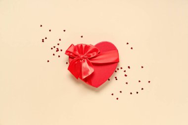 Kalp şeklinde bir hediye kutusu ve bej arka planda konfeti. Sevgililer Günü kutlaması