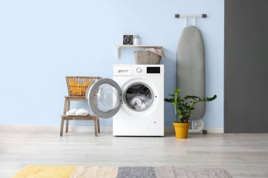 Çamaşır odasının içinde modern çamaşır makinesi ve ütü masası var.