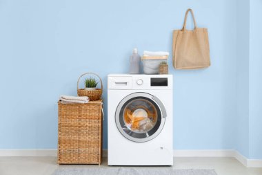 Çamaşır odasının içinde modern çamaşır makinesi ve sepeti açık mavi duvarın yanında.