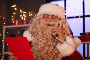 Elinde dosya olan Noel Baba postanede telefonla konuşuyor.