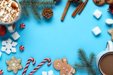 Lezzetli Noel kurabiyelerinden yapılmış çerçeve, marşmelovlu kakao, şeker kamışları, köknar dalları, kar tanesi ve mavi arka planda tarçın.
