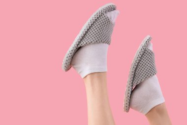 Pembe arka planda gri yumuşak terlikler giyen kadın bacakları.