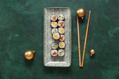 Lezzetli suşi ruloları ve yeşil arka planda Noel topları olan tabaklar.
