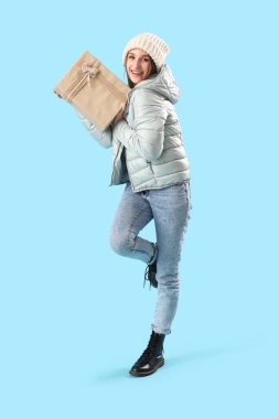 Mavi arka planda Noel hediyesi olan kışlık elbiseli genç bir kadın.