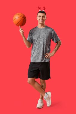 Kırmızı arka planda basketbol oynayan ren geyiği boynuzlu genç adam.