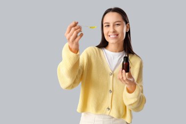 Gri arka planda boğaz ağrısı için şurubu olan genç bir kadın.