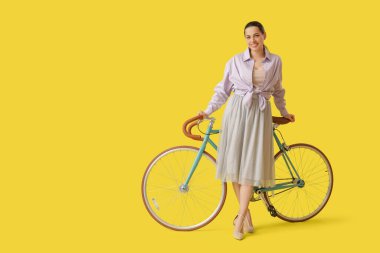 Happy young woman with bicycle on yellow background