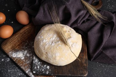 Tahta tahta, taze hamur, buğday ve yumurta ve siyah arka planda.