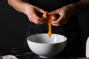 Adam siyah arka plana karşı masada taze hamur hazırlıyor.